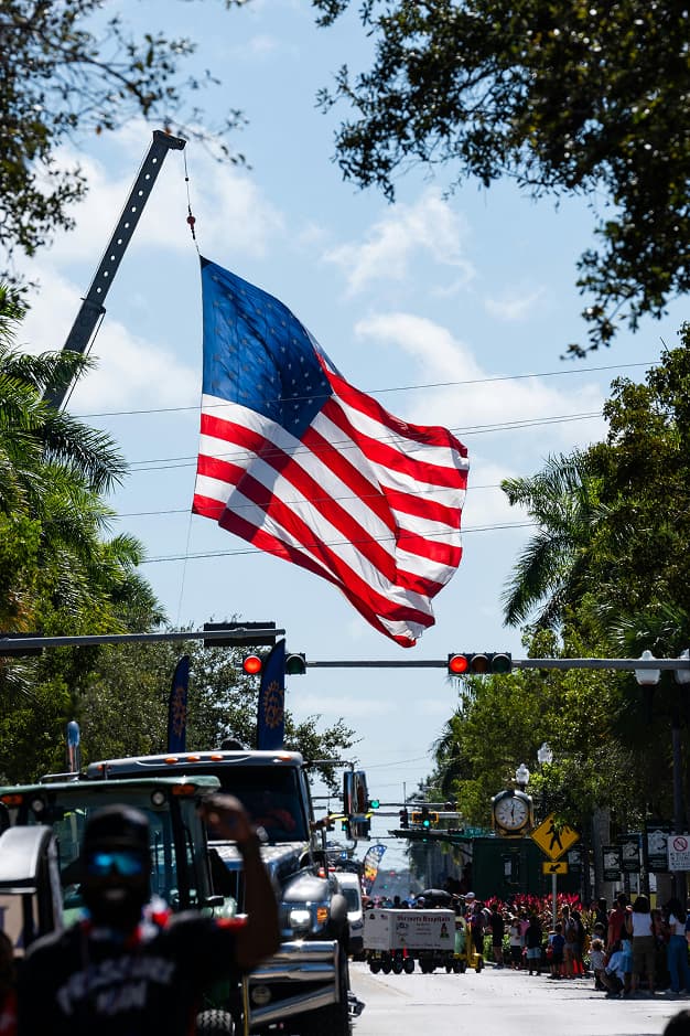 Gran bandera estadounidense ondeando en un desfile callejero, resaltando aspectos culturales y de movimiento logístico como los gestionados por Del Bravo Trade